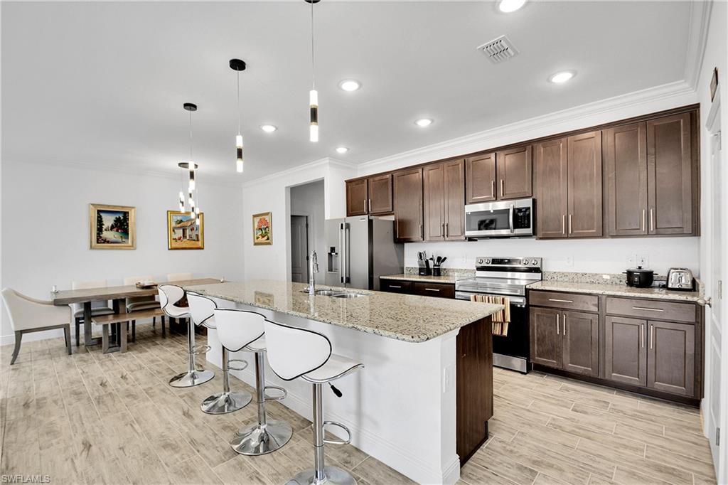 Kitchen with dark brown cabinetry, ornamental molding, appliances with stainless steel finishes, a breakfast bar, and light stone countertops