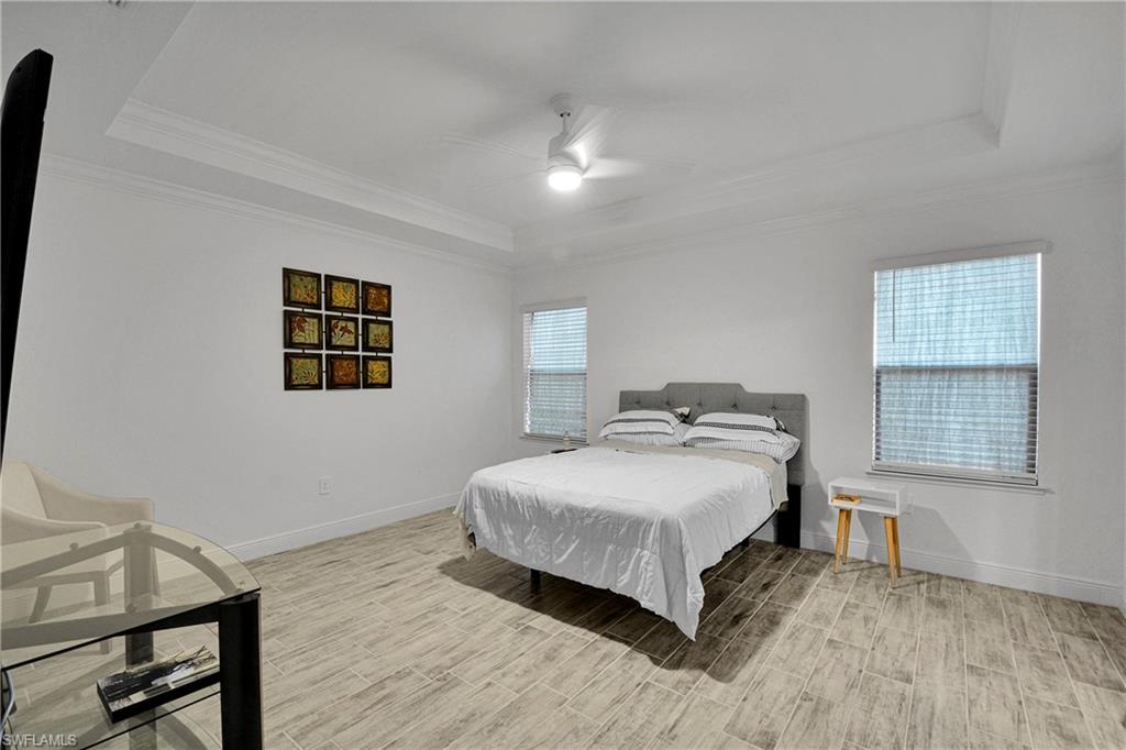 Bedroom with a raised ceiling, wood tiled floors, ceiling fan, and crown molding