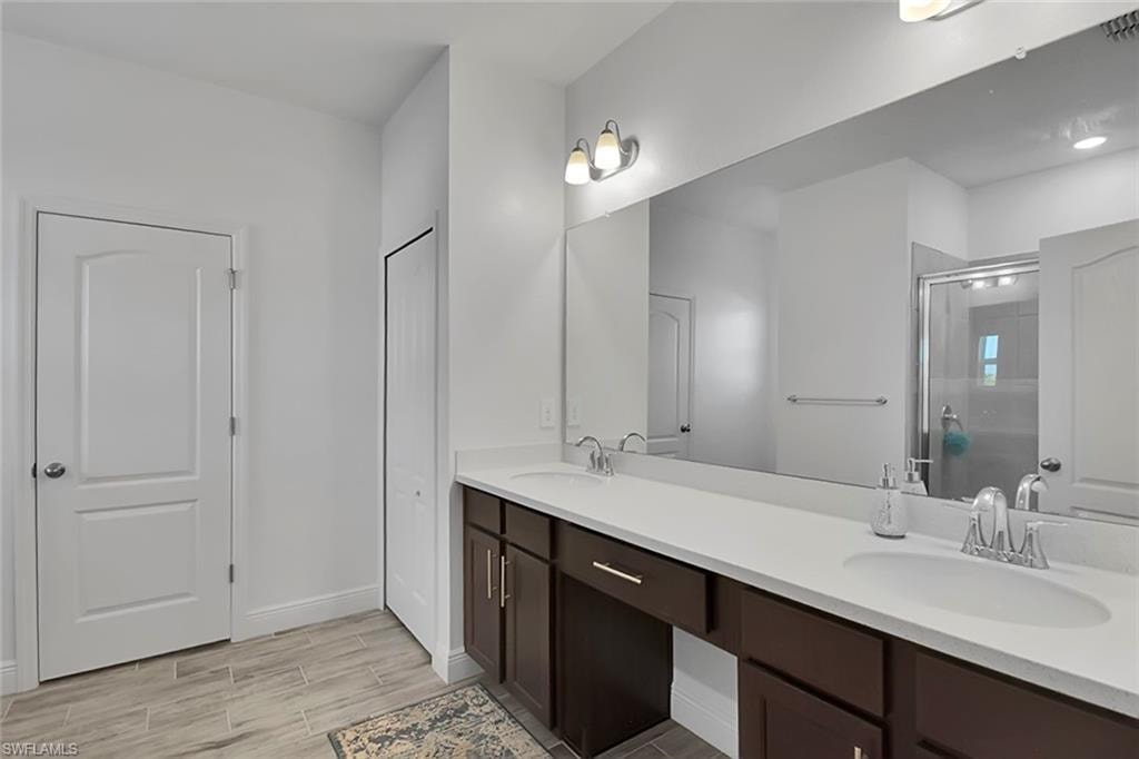 Full bathroom with double vanity, wood tiled floors, and a shower stall