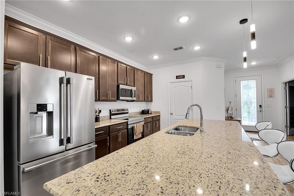 Kitchen with stainless steel appliances, ornamental molding, light stone countertops, dark brown cabinets, and recessed lighting