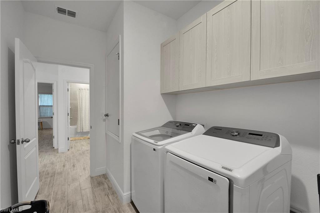 Laundry area with light wood finished floors, washer and dryer, and cabinet space