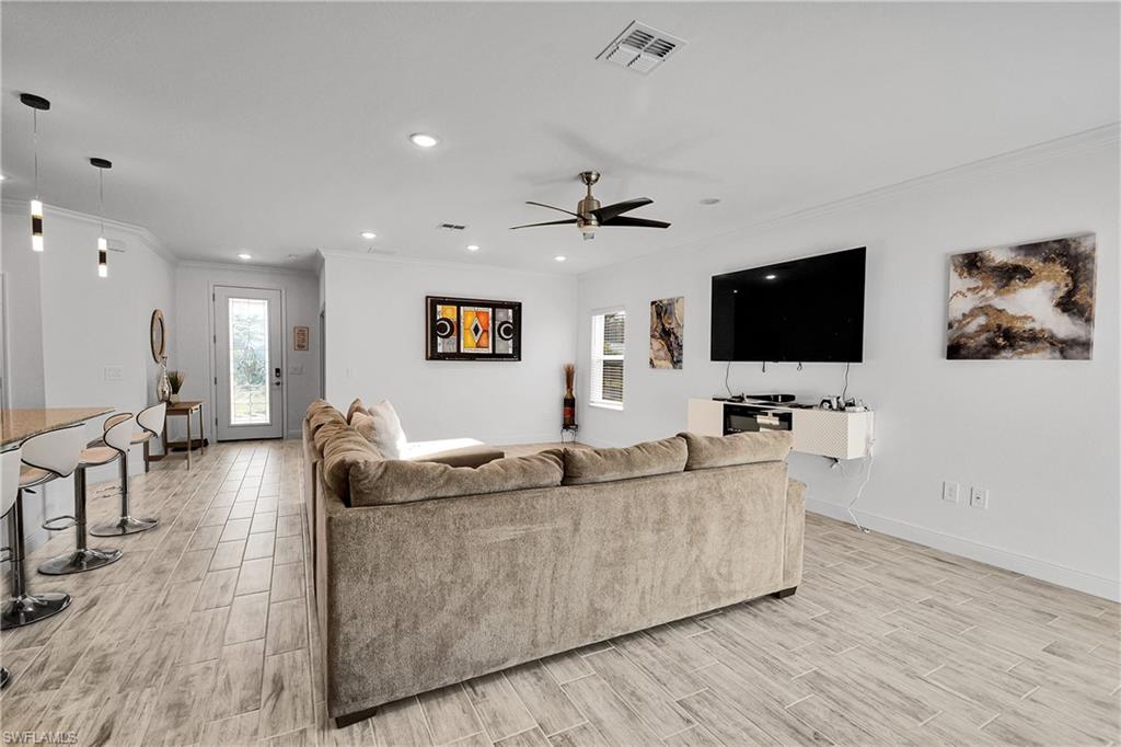 Living area with ornamental molding, wood tiled floors, healthy amount of natural light, ceiling fan, and recessed lighting