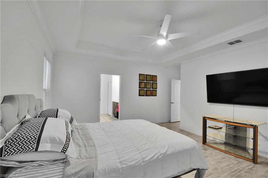 Bedroom with a raised ceiling, crown molding, a ceiling fan, light wood-style floors, and ensuite bath