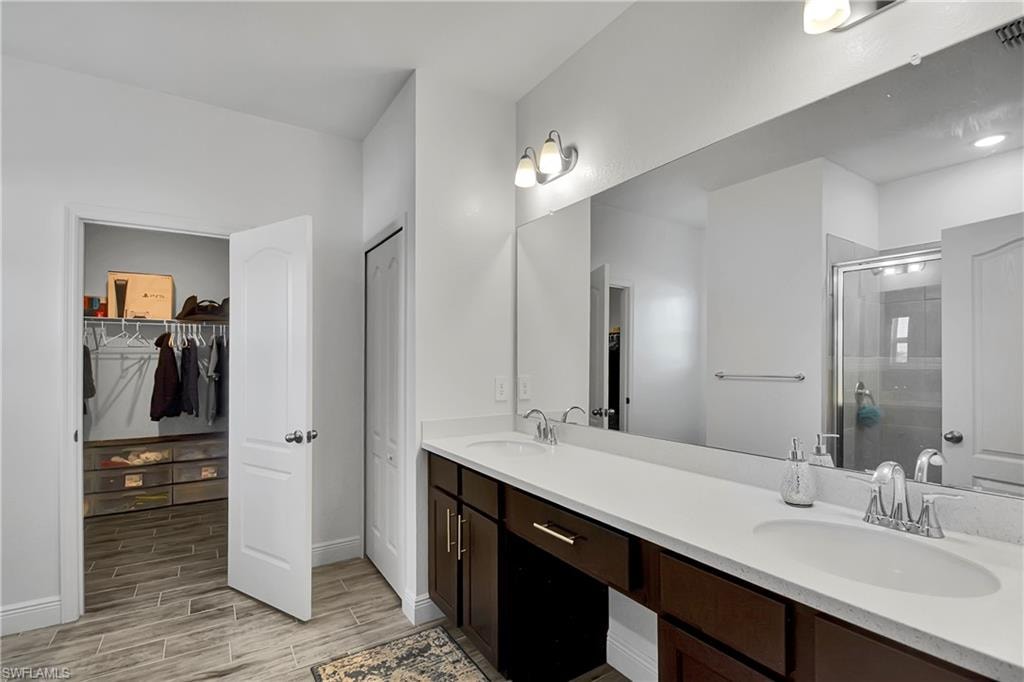 Full bathroom featuring double vanity, a spacious closet, a shower stall, and wood finish floors