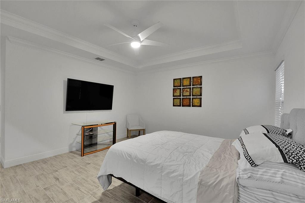 Bedroom featuring a tray ceiling, ceiling fan, ornamental molding, and wood finish floors