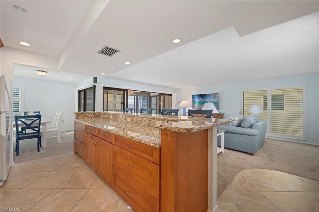 Kitchen featuring light carpet, brown cabinets, light stone counters, open floor plan, and light tile patterned floors