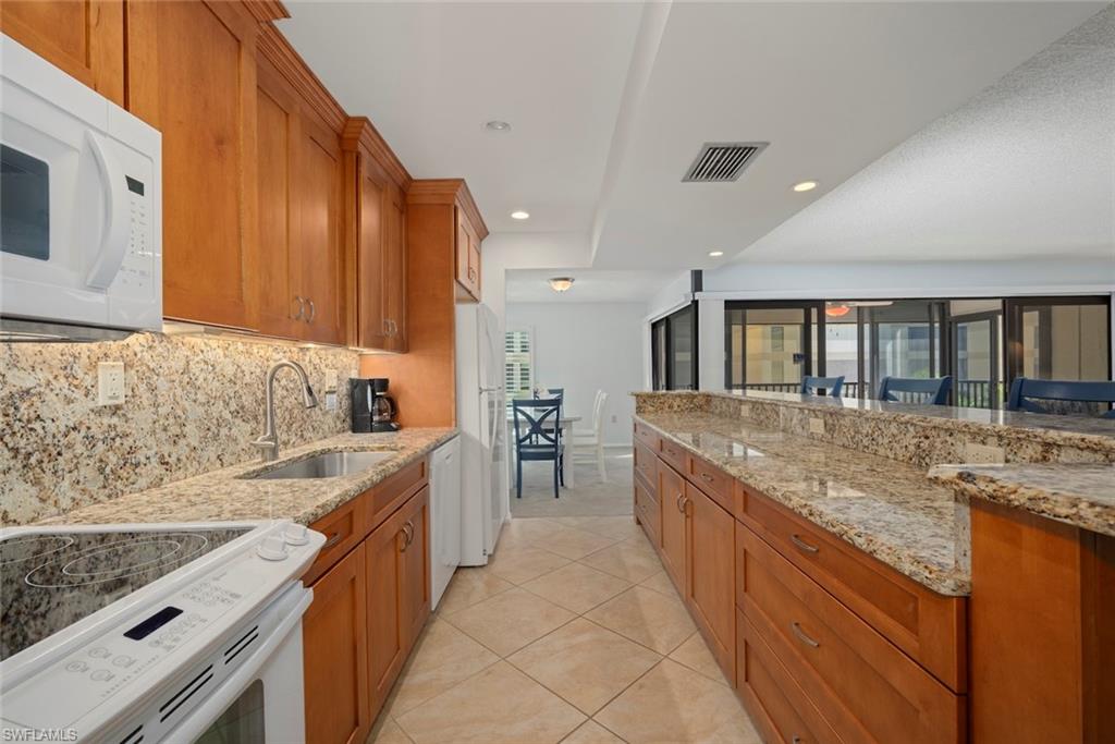 Kitchen with white appliances, brown cabinets, light stone countertops, and recessed lighting