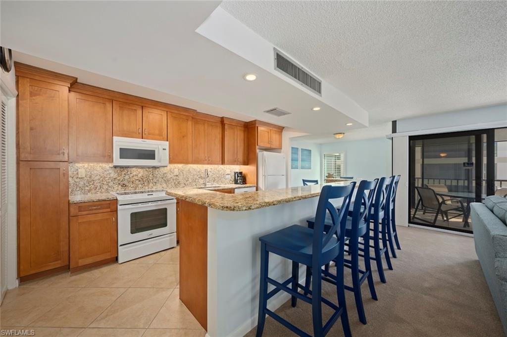 Kitchen featuring a breakfast bar area, light stone countertops, white appliances, tasteful backsplash, and recessed lighting