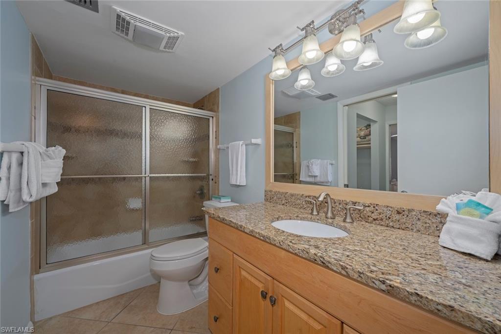 Bathroom featuring vanity, light tile patterned flooring, combined bath / shower with glass door, and a walk in closet