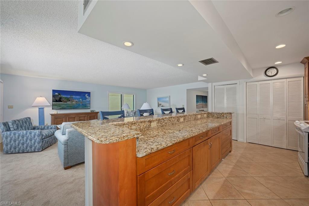 Kitchen featuring light stone countertops, brown cabinets, open floor plan, a center island, and range with electric cooktop