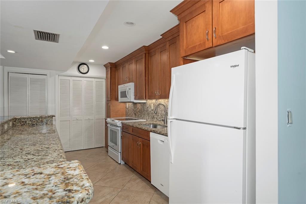 Kitchen with white appliances, light stone countertops, light tile patterned flooring, brown cabinets, and decorative backsplash