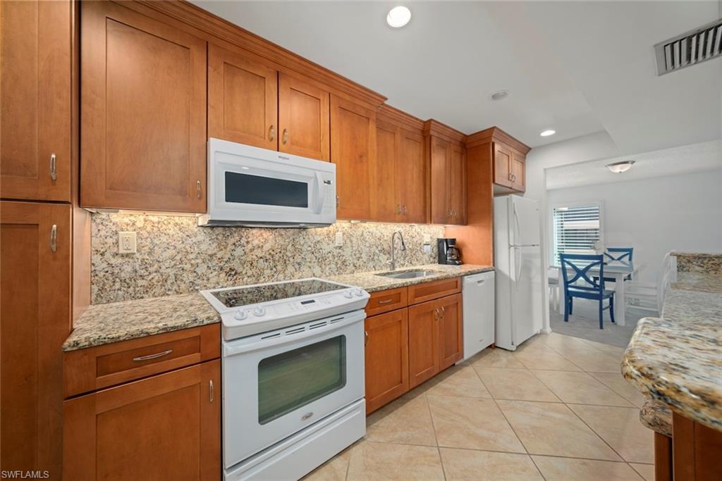 Kitchen with white appliances, brown cabinets, light stone countertops, backsplash, and light tile patterned flooring