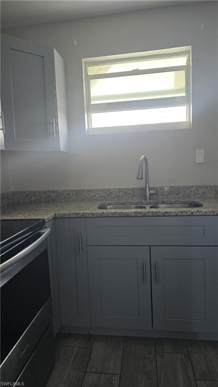 Kitchen with stainless steel range with electric cooktop, light stone countertops, gray cabinets, and dark wood finished floors