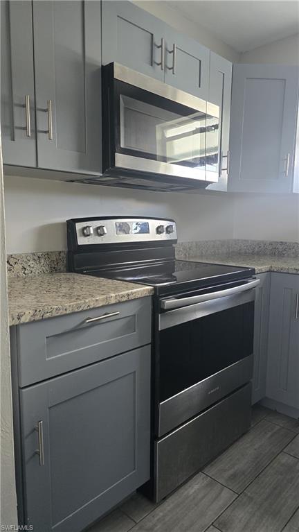 Kitchen with stainless steel appliances, gray cabinets, light stone countertops, and light wood finished floors
