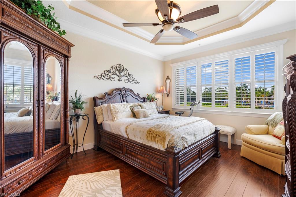 Bedroom featuring a tray ceiling, crown molding, dark wood-type flooring, and ceiling fan