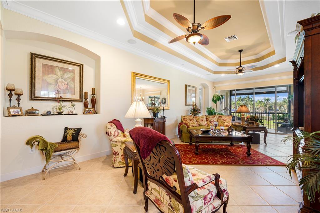 Living area with a raised ceiling, ornamental molding, light tile patterned floors, and ceiling fan