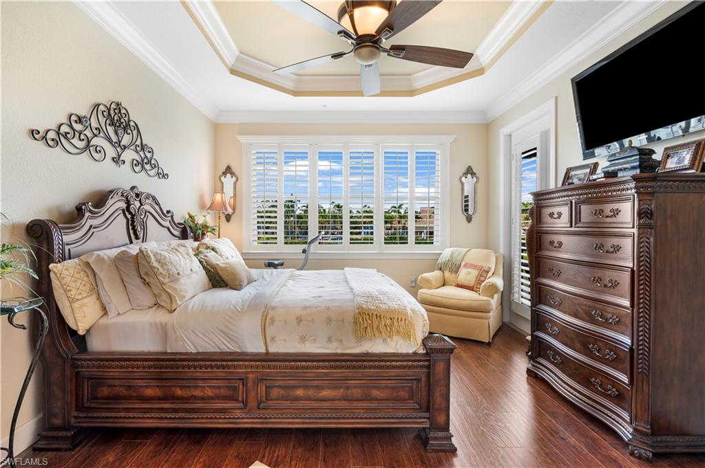 Bedroom featuring a raised ceiling, crown molding, dark wood-style floors, and a ceiling fan