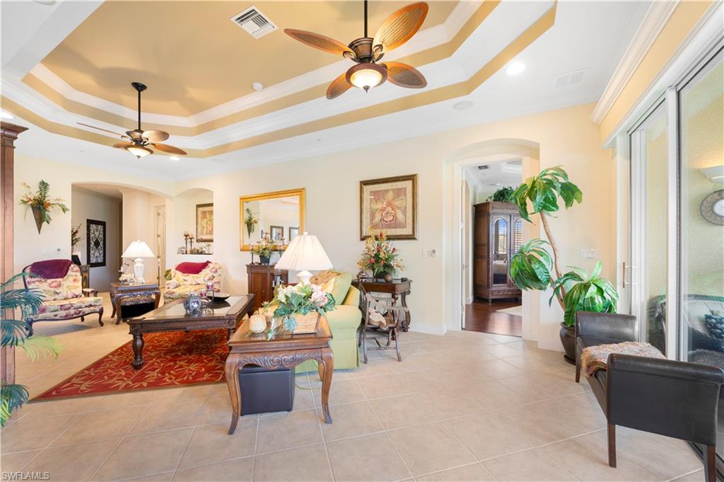 Living room featuring a raised ceiling, crown molding, arched walkways, and ceiling fan