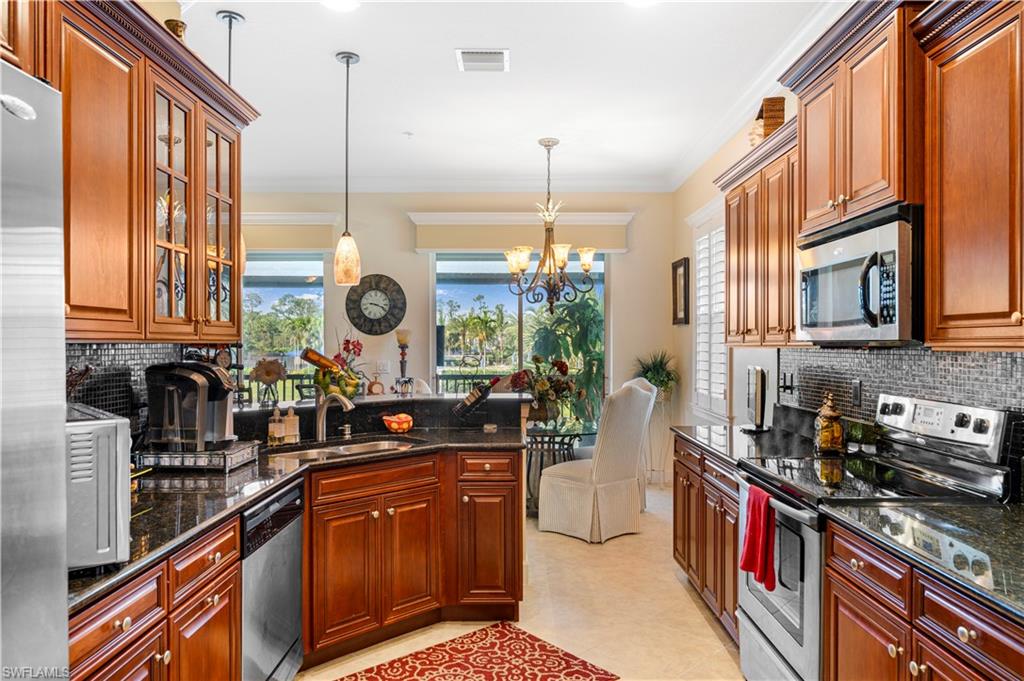 Kitchen with backsplash, appliances with stainless steel finishes, a chandelier, dark stone countertops, and crown molding
