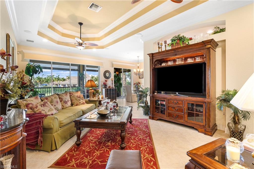 Living room featuring a tray ceiling, crown molding, a ceiling fan, light tile patterned flooring, and a chandelier