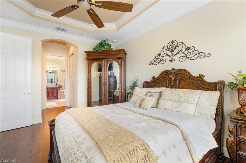 Bedroom featuring arched walkways, a tray ceiling, dark wood-type flooring, crown molding, and ensuite bath