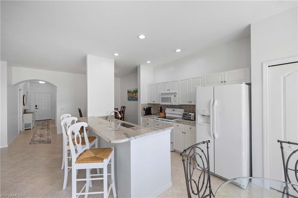 Kitchen with white appliances, backsplash, white cabinets, sink, and light stone countertops