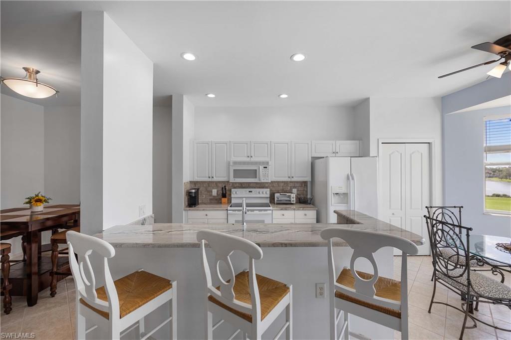 Kitchen featuring white appliances, decorative backsplash, light stone counters, white cabinetry, and a breakfast bar area
