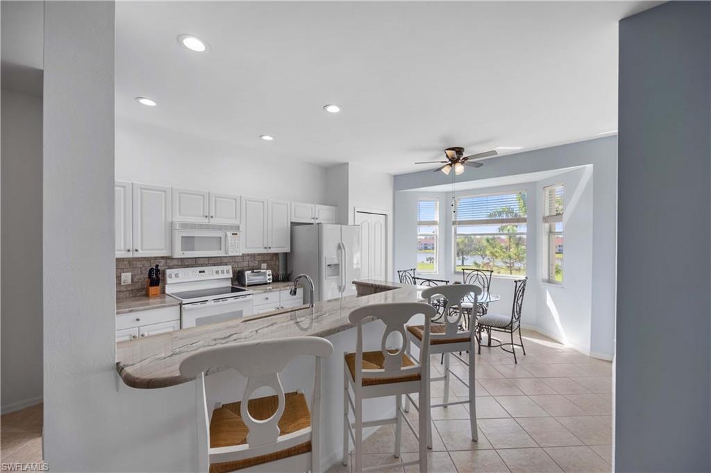 Kitchen featuring white cabinetry, light stone counters, white appliances, a kitchen bar, and decorative backsplash