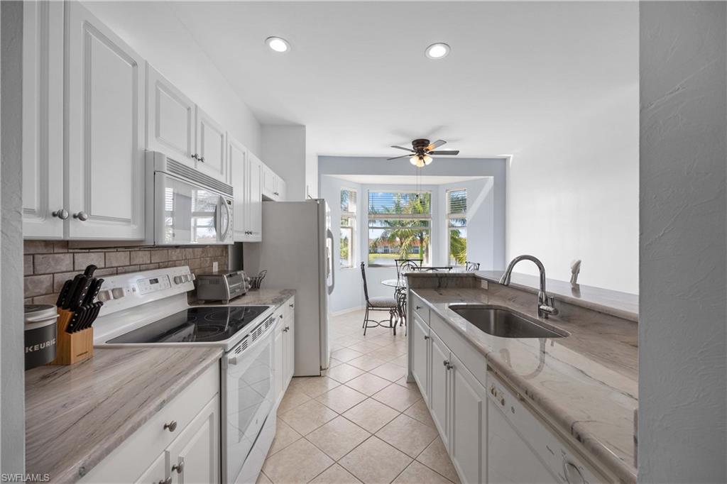 Kitchen with white appliances, sink, ceiling fan, tasteful backsplash, and white cabinetry
