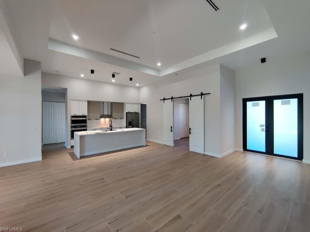 Unfurnished living room featuring a barn door, a raised ceiling, light wood-style floors, and recessed lighting