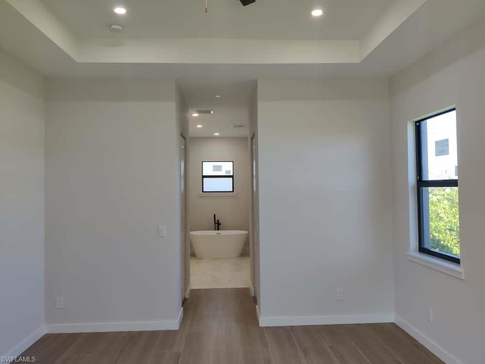Full bathroom featuring a tray ceiling, a freestanding bath, light wood-type flooring, recessed lighting, and a ceiling fan