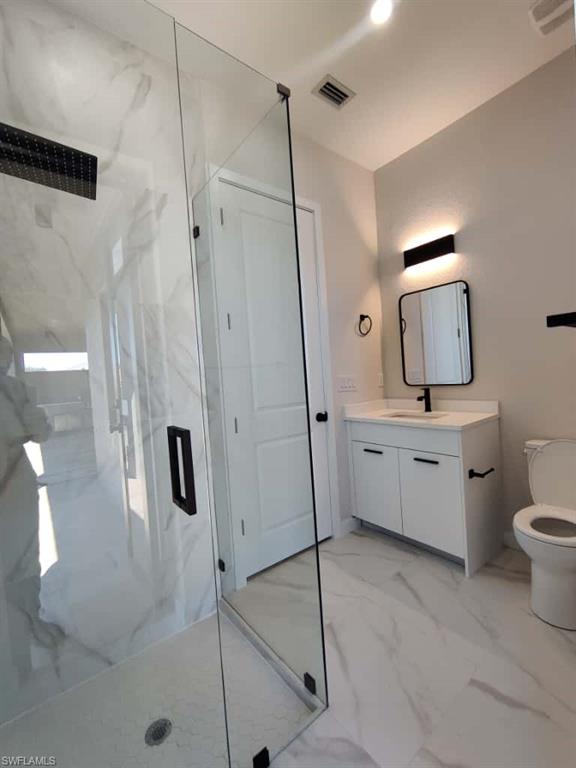 Bathroom with vanity, a marble finish shower, and light marble finish floors