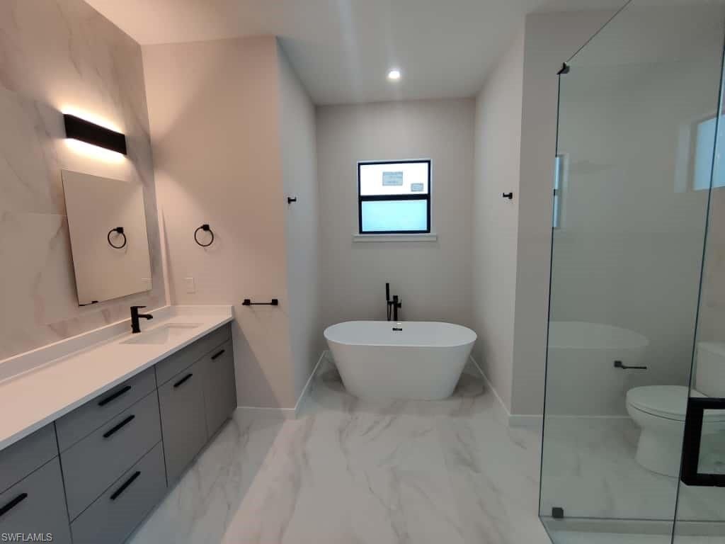 Bathroom featuring vanity, a soaking tub, an enclosed shower, light marble finish floors, and recessed lighting