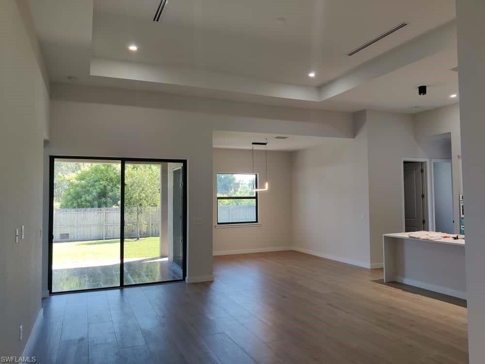 Empty room featuring a raised ceiling, light wood-style flooring, recessed lighting, and a chandelier