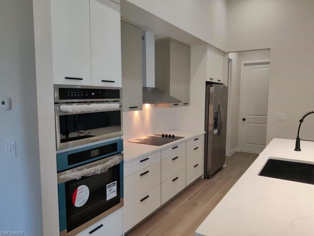 Kitchen with wall chimney exhaust hood, light wood-type flooring, white cabinets, and appliances with stainless steel finishes