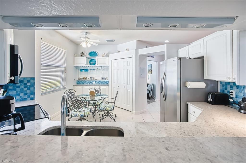 Kitchen with decorative backsplash, white cabinetry, stainless steel appliances, light stone countertops, and a ceiling fan
