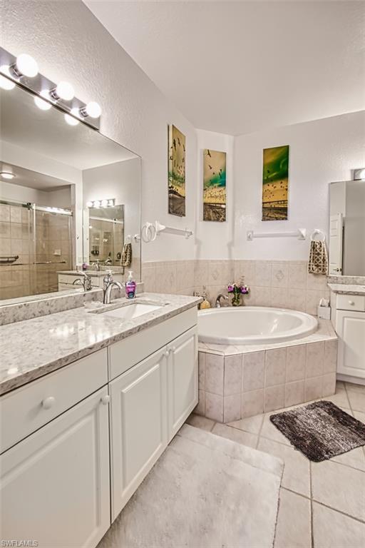 Full bathroom featuring two vanities, a stall shower, light tile patterned flooring, a textured wall, and a garden tub