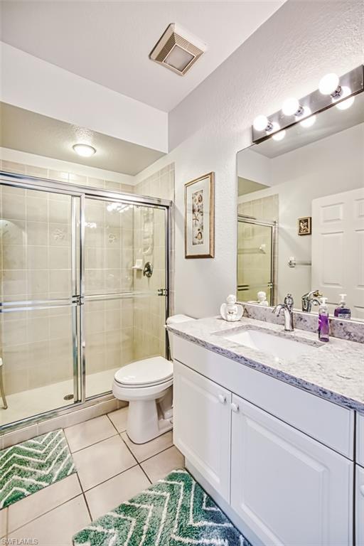 Full bath featuring vanity, light tile patterned flooring, a stall shower, and a textured wall