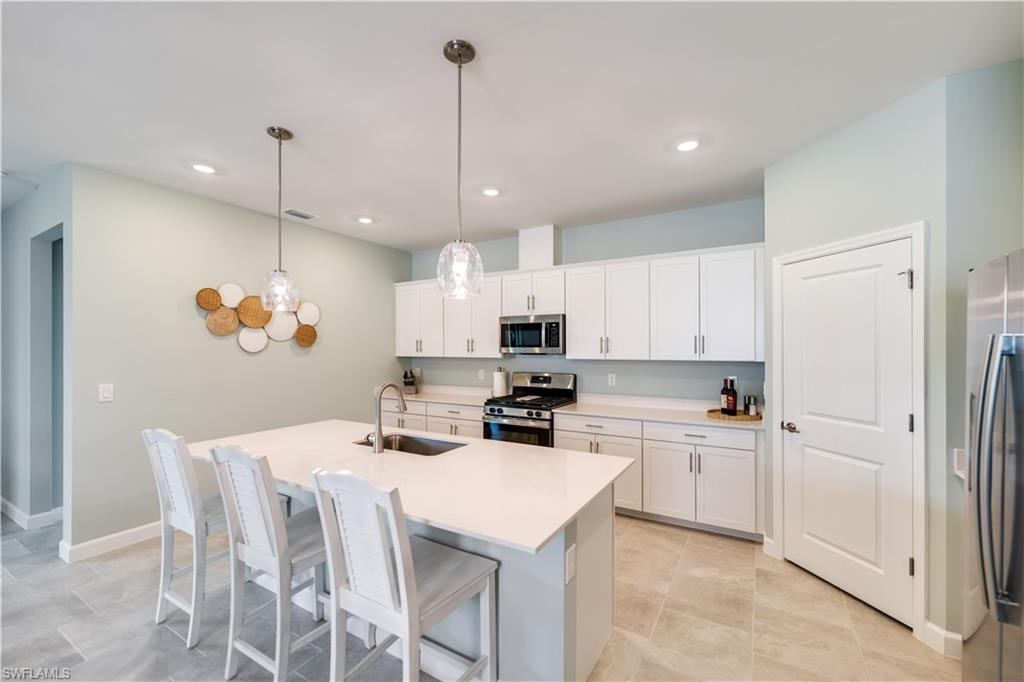 Kitchen featuring stainless steel appliances, white cabinets, sink, hanging light fixtures, and an island with sink