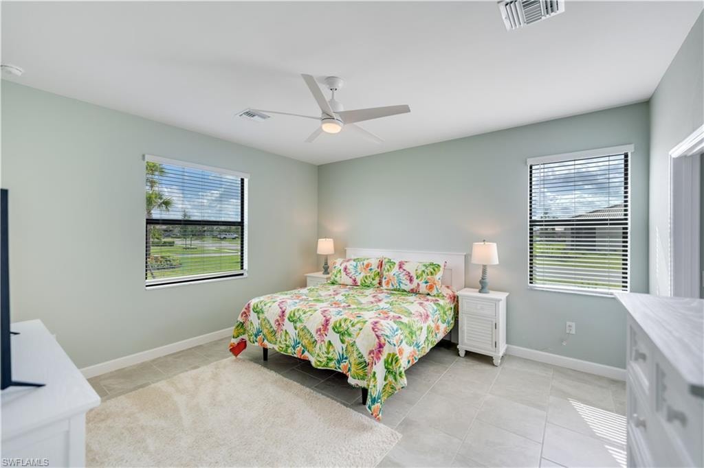 Tiled bedroom featuring multiple windows and ceiling fan