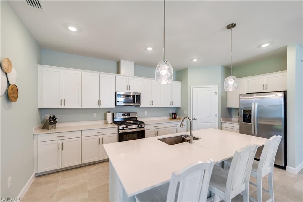 Kitchen featuring a center island with sink, decorative light fixtures, appliances with stainless steel finishes, and sink
