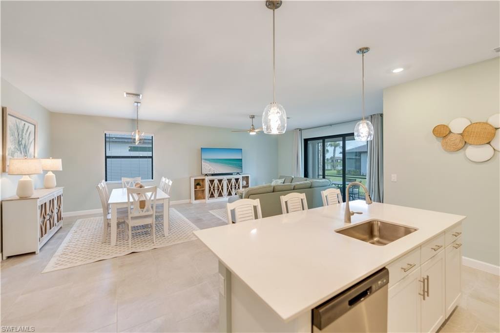 Kitchen with white cabinetry, a kitchen island with sink, stainless steel dishwasher, decorative light fixtures, and sink