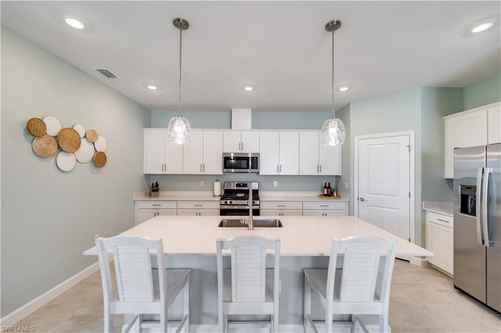Kitchen featuring light tile patterned flooring, appliances with stainless steel finishes, decorative light fixtures, and white cabinetry