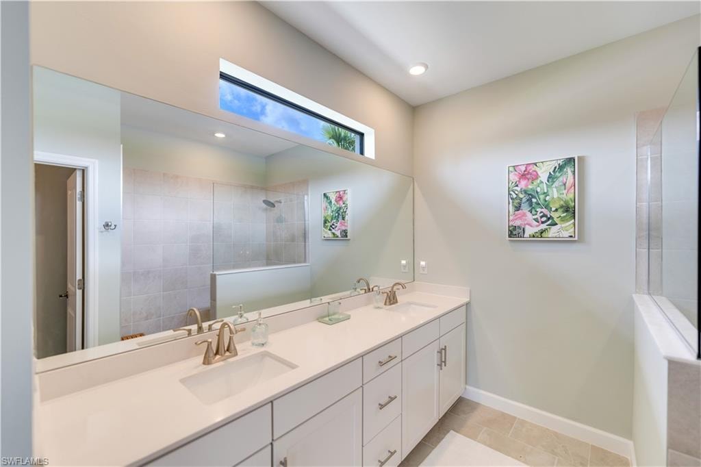 Bathroom with tile patterned flooring, tiled shower, and dual bowl vanity
