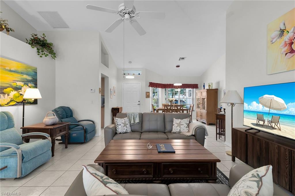 Living room with light tile patterned flooring, ceiling fan, and vaulted ceiling