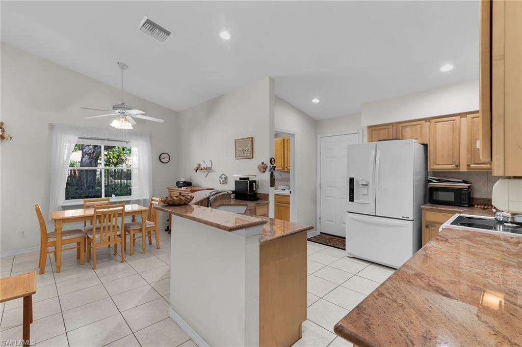Kitchen with white fridge with ice dispenser, lofted ceiling, light tile patterned flooring, a peninsula, and light stone countertops