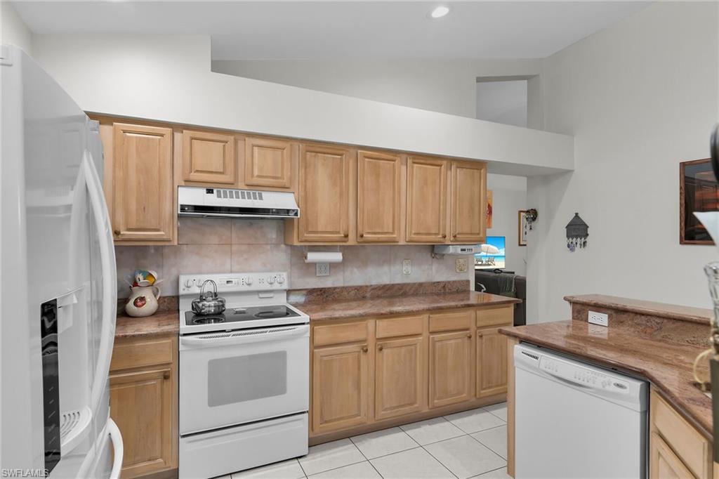 Kitchen featuring white appliances, decorative backsplash, light tile patterned flooring, dark stone countertops, and exhaust hood
