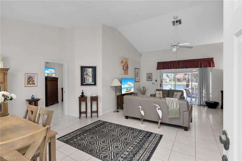 Living room with high vaulted ceiling, healthy amount of natural light, light tile patterned floors, and a ceiling fan