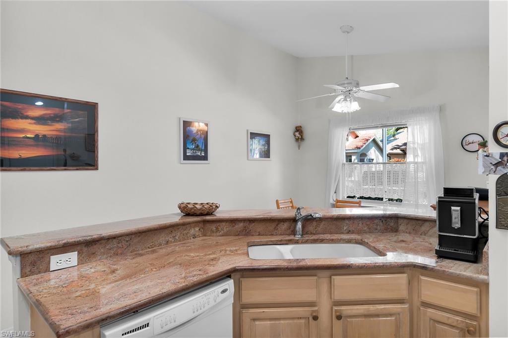 Kitchen with dishwasher, light stone countertops, a ceiling fan, vaulted ceiling, and light brown cabinetry