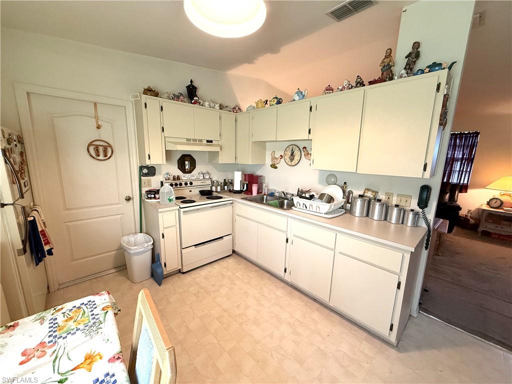 Kitchen with white appliances, light countertops, ventilation hood, light floors, and lofted ceiling